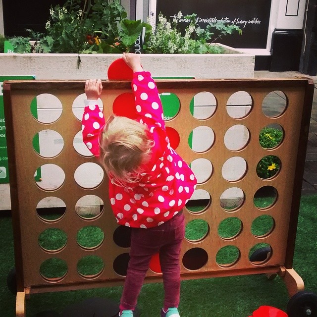 A young child reaching up to place a large disc in a child-height Connect Four board